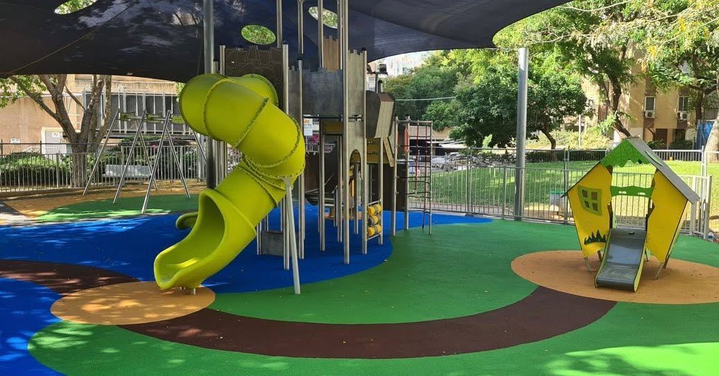 מגלשה צהובה מתפתלת במתקן משחקים תחת הצללה