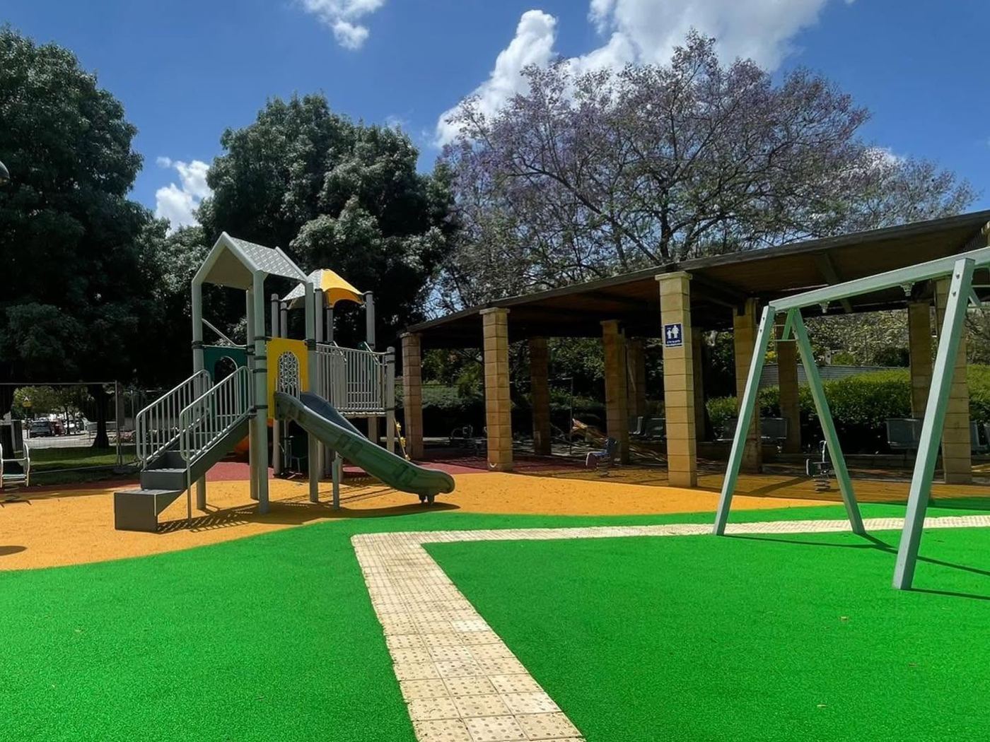 שביל נגישות מרוצף בגן משחקים מוצל, עם ישיבה מוצלת ברקע