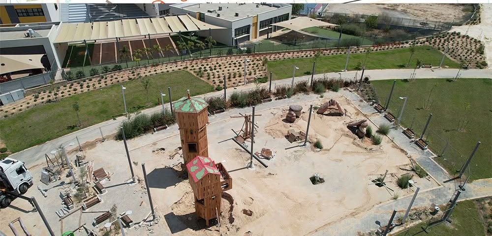 צילום אווירי של גן משחקים עם מגדלי עץ וגבעת חול בשלבי גימור