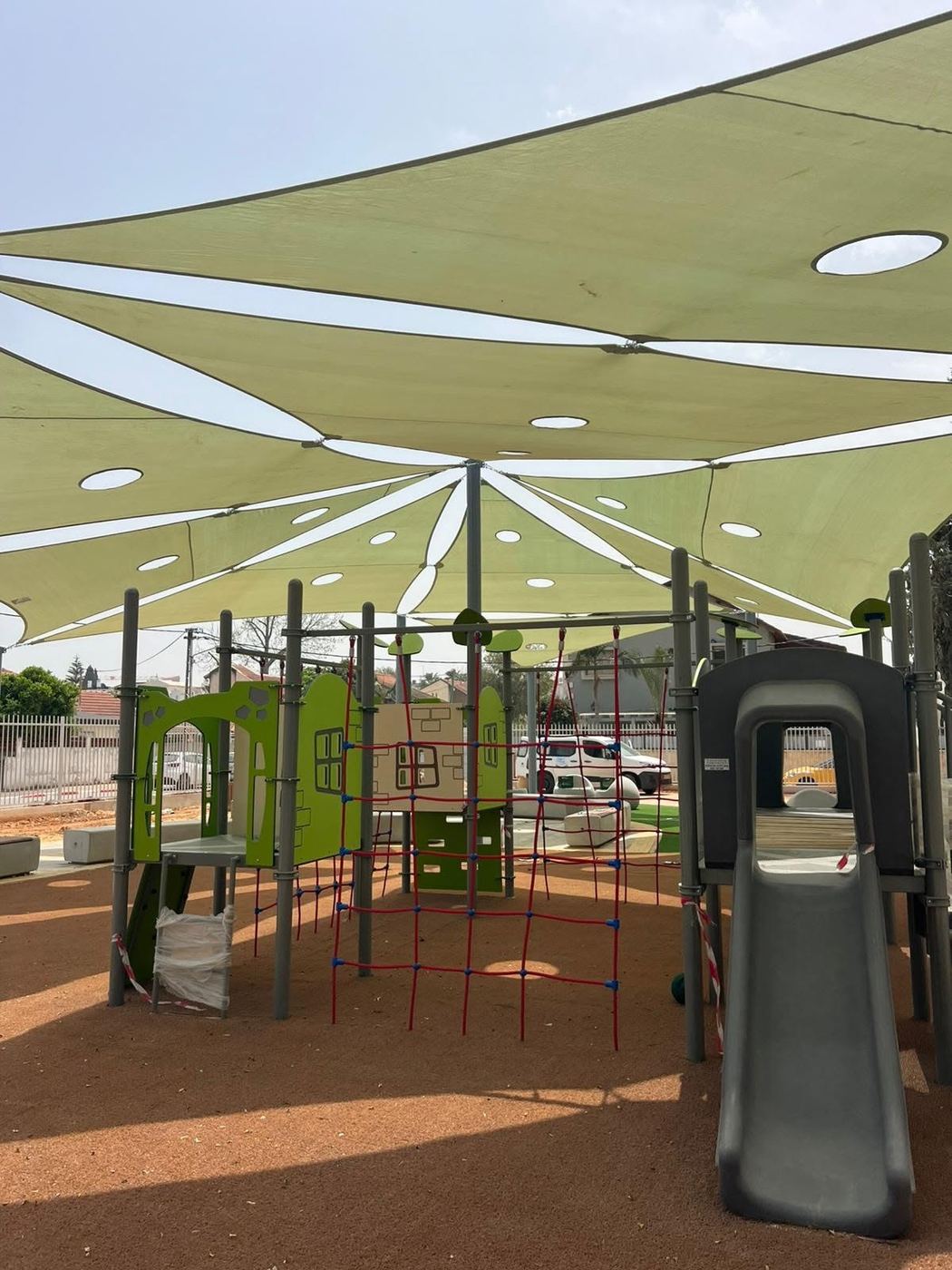 מתקן טיפוס רשת אדום תחת מפרשי הצללה ירוקים