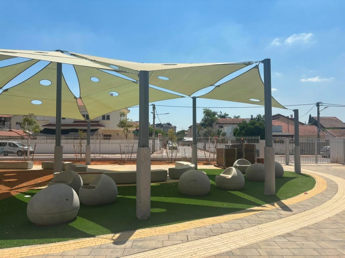 מושבי בטון בצורת ביצה על דשא סינטטי, תחת מפרשי הצללה